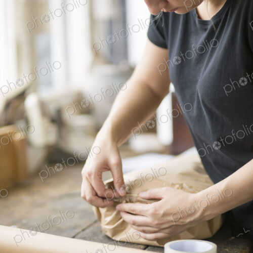 Woman standing in a workshop sealing a package wrapped in brown packaging paper with… Woman standing in a workshop sealing a package wrapped in brown packaging paper with…