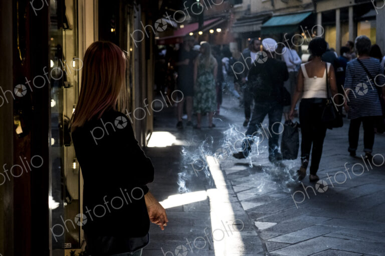 Woman standing in narrow street in Venice, Veneto, Italy, smoking a cigarette.