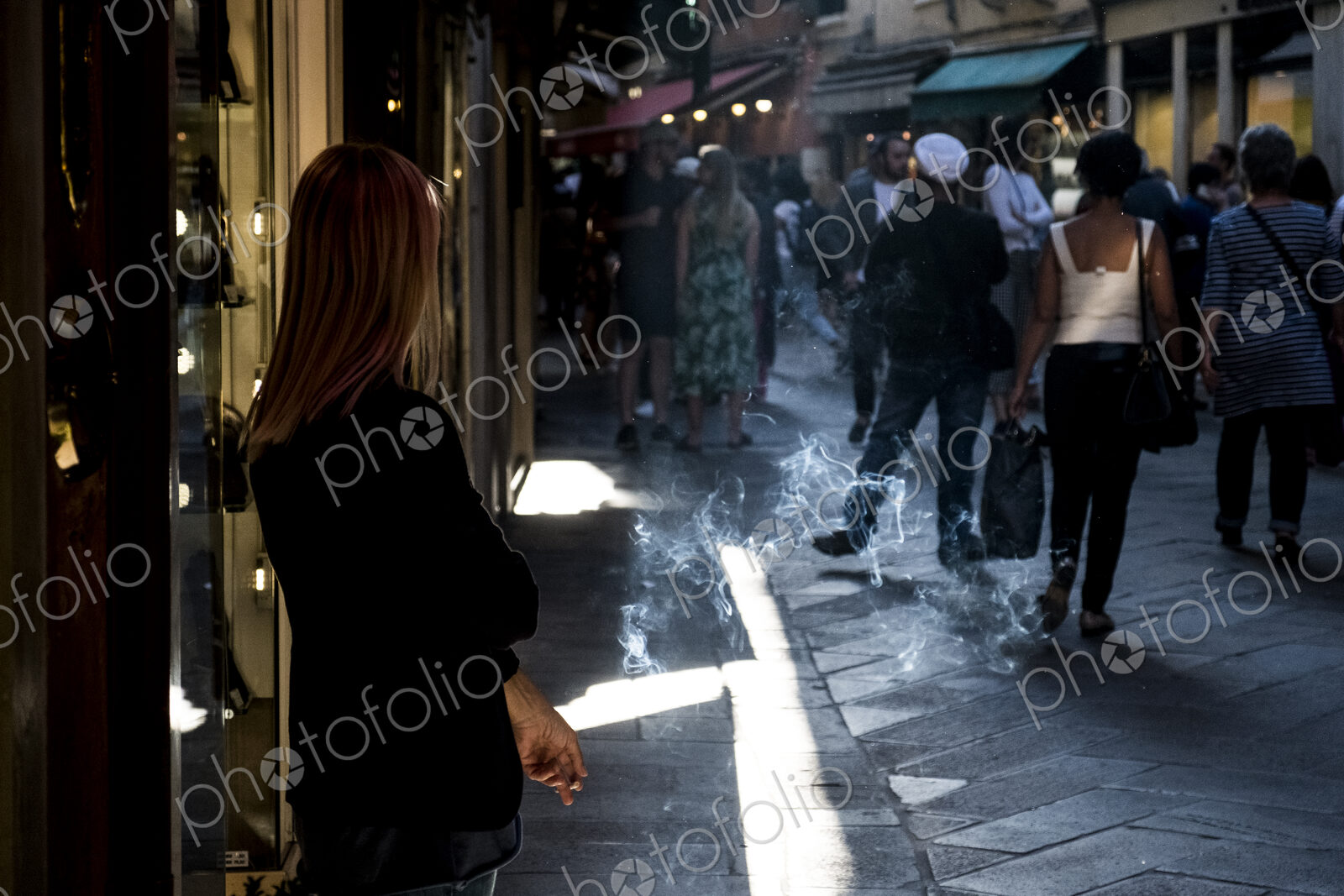Woman standing in narrow street in Venice, Veneto, Italy, smoking a cigarette.
