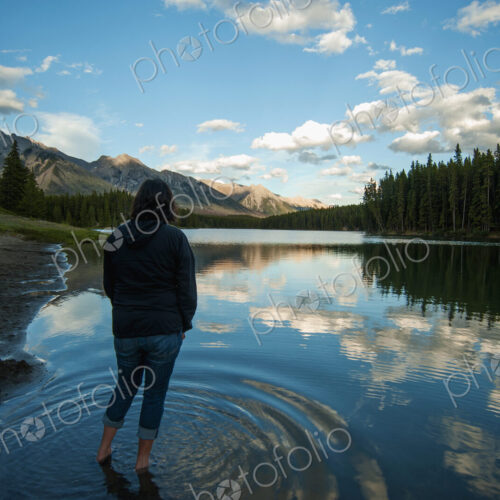 Woman standing in shallow water of Johnson Lake in Banff National Park looking at…