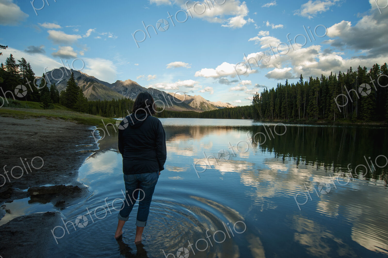 Woman standing in shallow water of Johnson Lake in Banff National Park looking at…