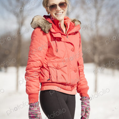 Woman standing in snow wearing red parka and sunglasses.