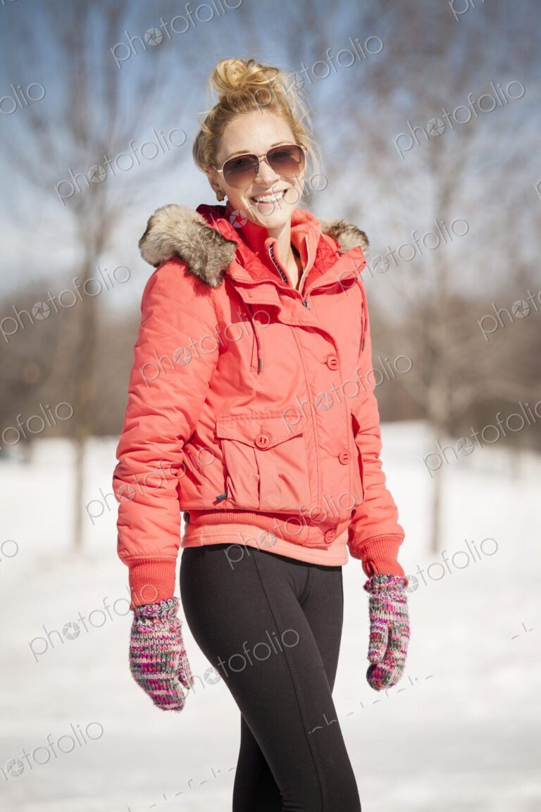 Woman standing in snow wearing red parka and sunglasses.