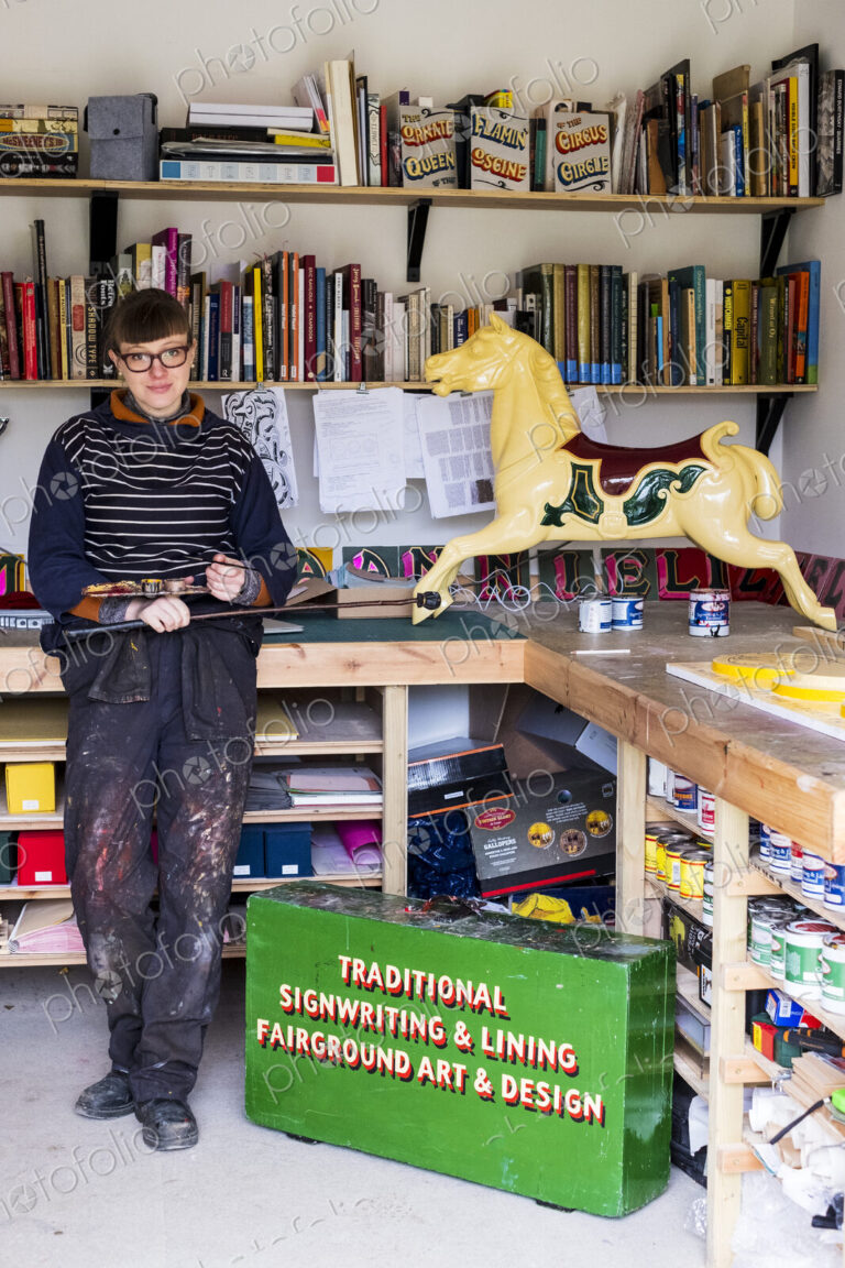 Woman standing in workshop next to traditional wooden horse from merry-go-round,…