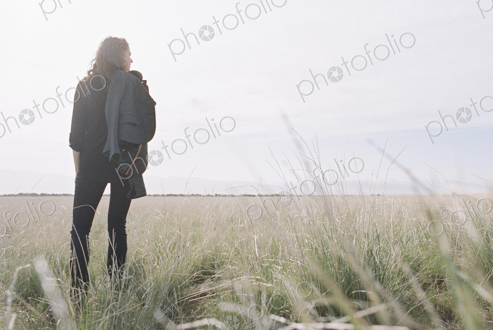 Woman standing looking to the horizon, carrying a jacket and backpack.