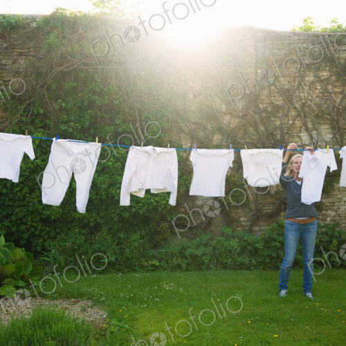 Woman standing on a lawn in a garden, hanging up laundry on washing line. Woman standing on a lawn in a garden, hanging up laundry on washing line.