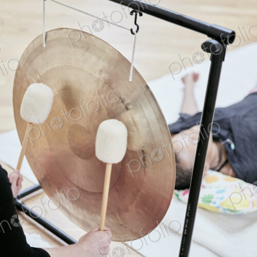 Woman striking a large gong wit soft drumsticks during a sound therapy session