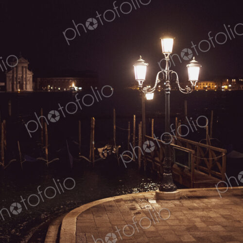 Woman taking picture of a streetlight by a lagoon in Venice, Veneto, Italy, at night.
