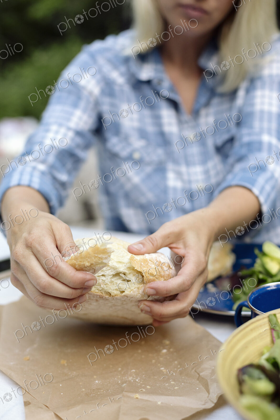 Woman tearing off a piece from a loaf of white bread.