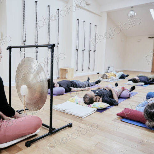 Woman using a gong during a sound therapy session and three people lying on their…