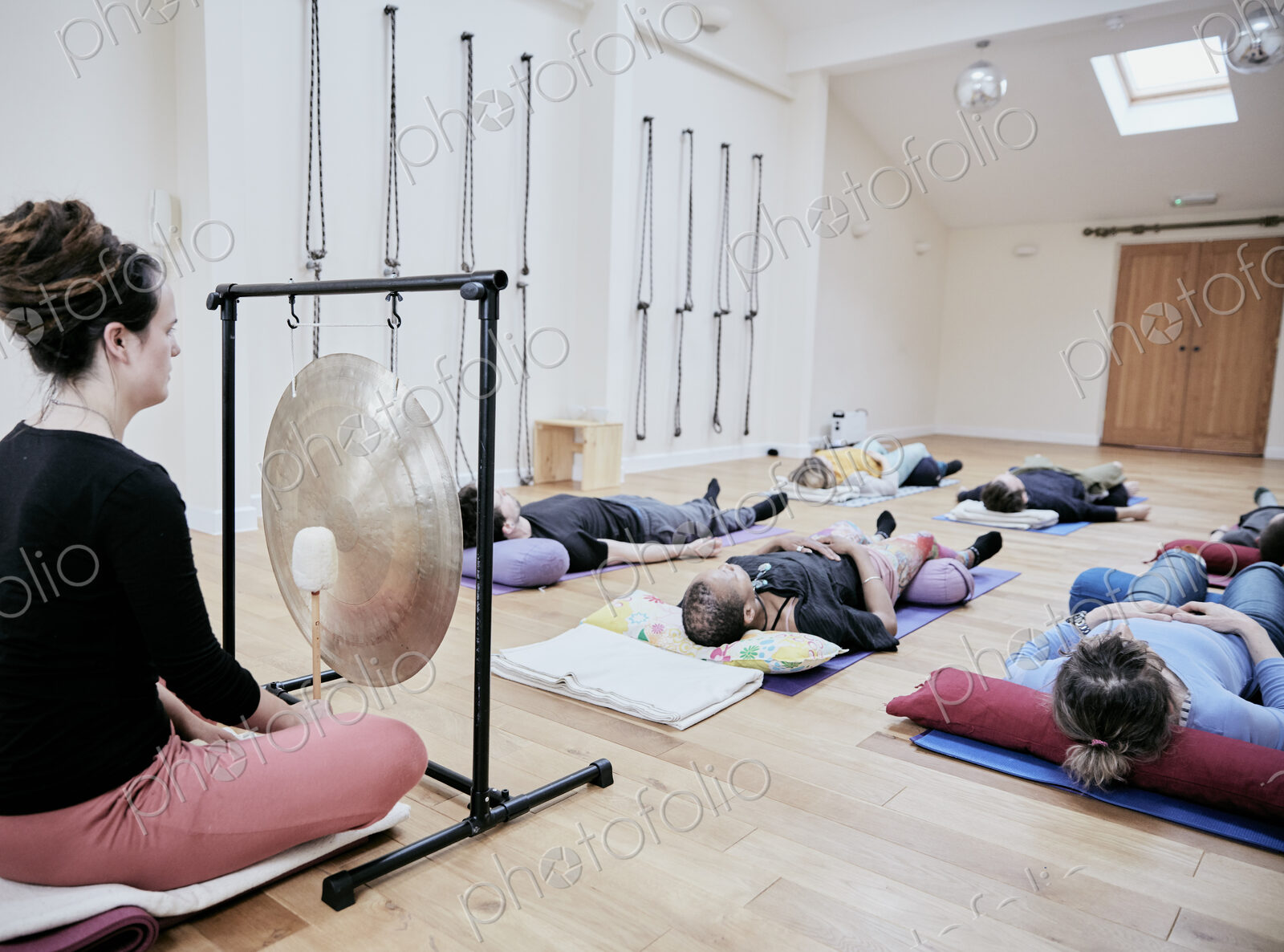 Woman using a gong during a sound therapy session and three people lying on their…
