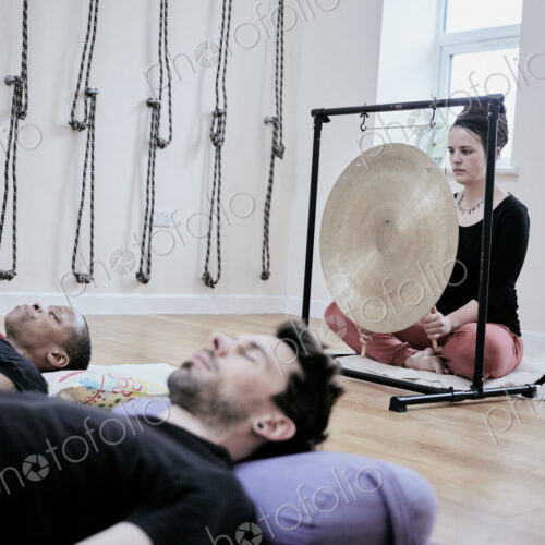 Woman using a gong during a sound therapy session and three people lying on their…
