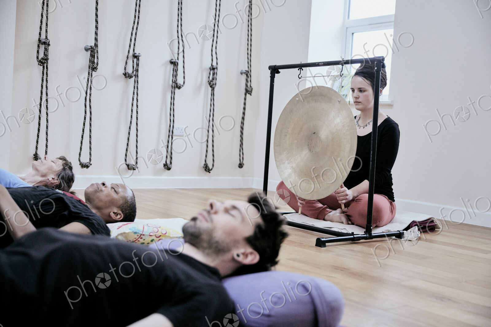 Woman using a gong during a sound therapy session and three people lying on their…