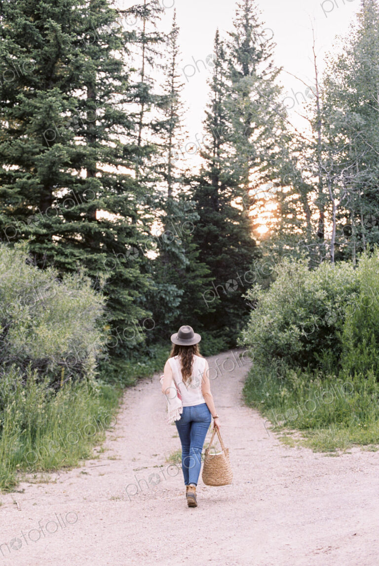 Woman walking along a forest path, carrying a bag.