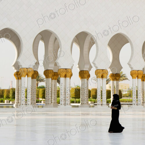 Woman walking past colonnade of mosque with white washed and golden columns. Woman walking past colonnade of mosque with white washed and golden columns.