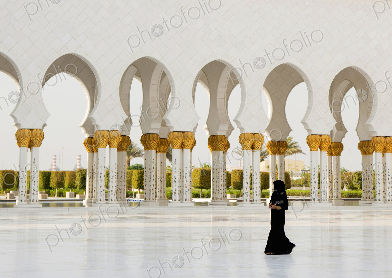 Woman walking past colonnade of mosque with white washed and golden columns.