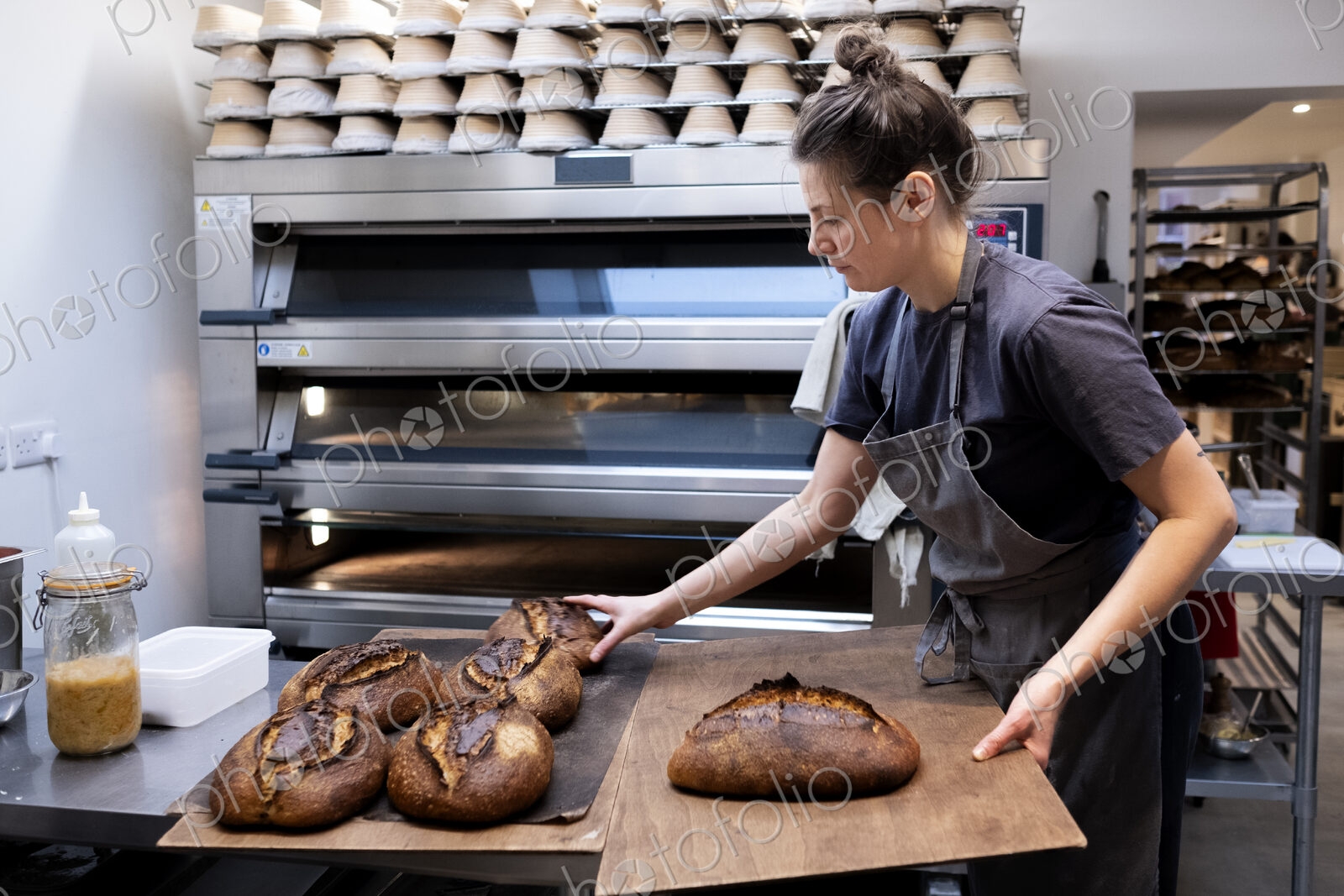 Woman wearing apron standing in an artisan bakery, placing freshly baked loaves of…