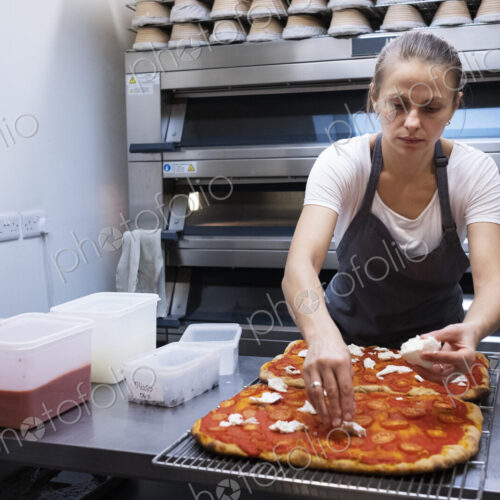 Woman wearing apron standing in an artisan bakery, preparing pizza.
