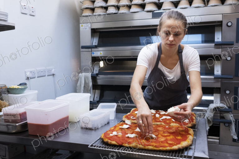 Woman wearing apron standing in an artisan bakery, preparing pizza.