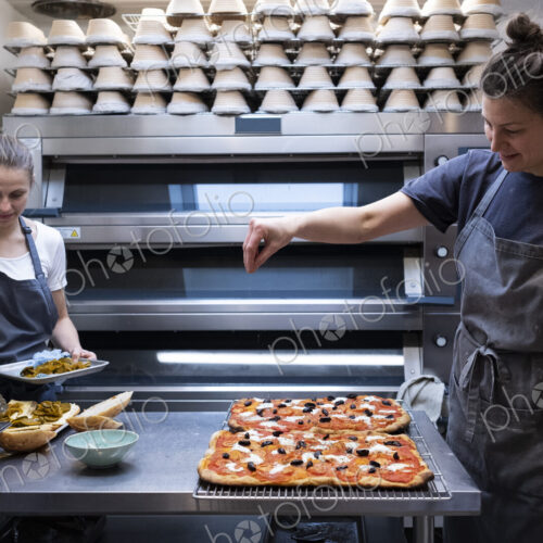 Woman wearing apron standing in an artisan bakery, preparing pizza.