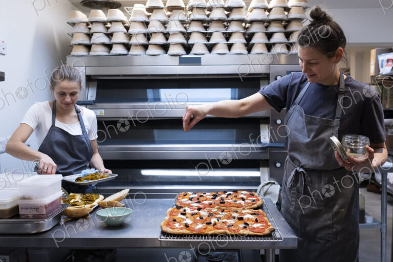 Woman wearing apron standing in an artisan bakery, preparing pizza.
