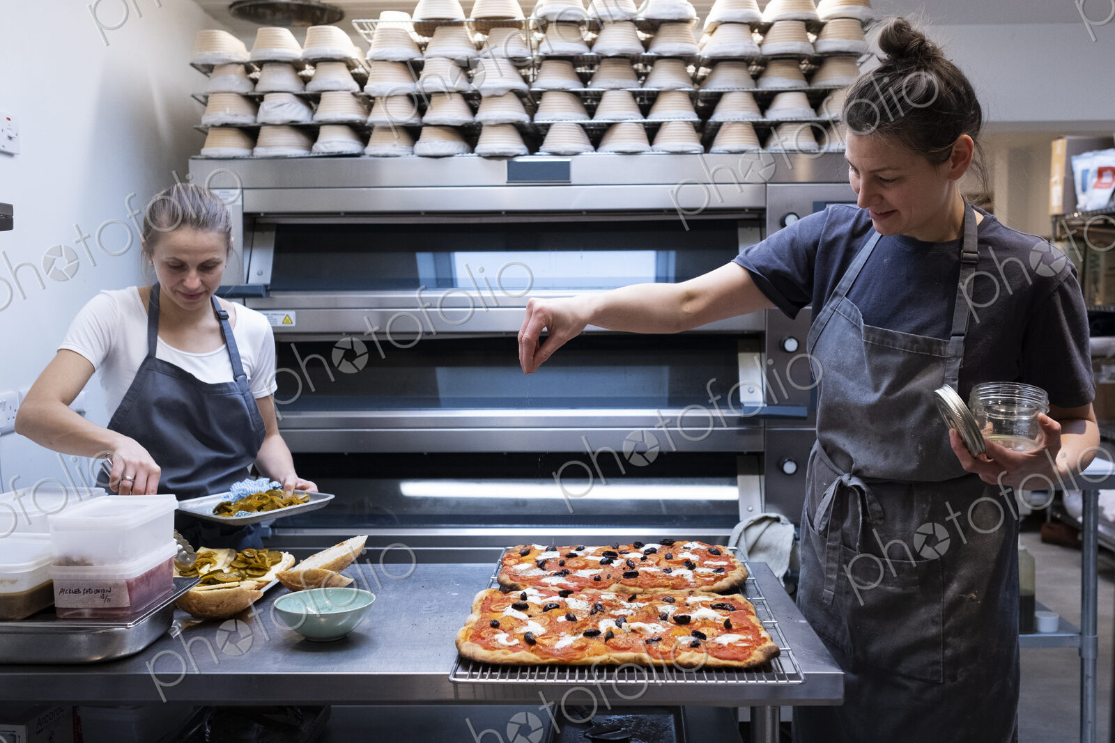 Woman wearing apron standing in an artisan bakery, preparing pizza.