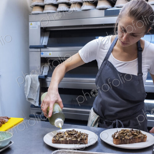 Woman wearing apron standing in an artisan bakery, preparing plate of food. Woman wearing apron standing in an artisan bakery, preparing plate of food.