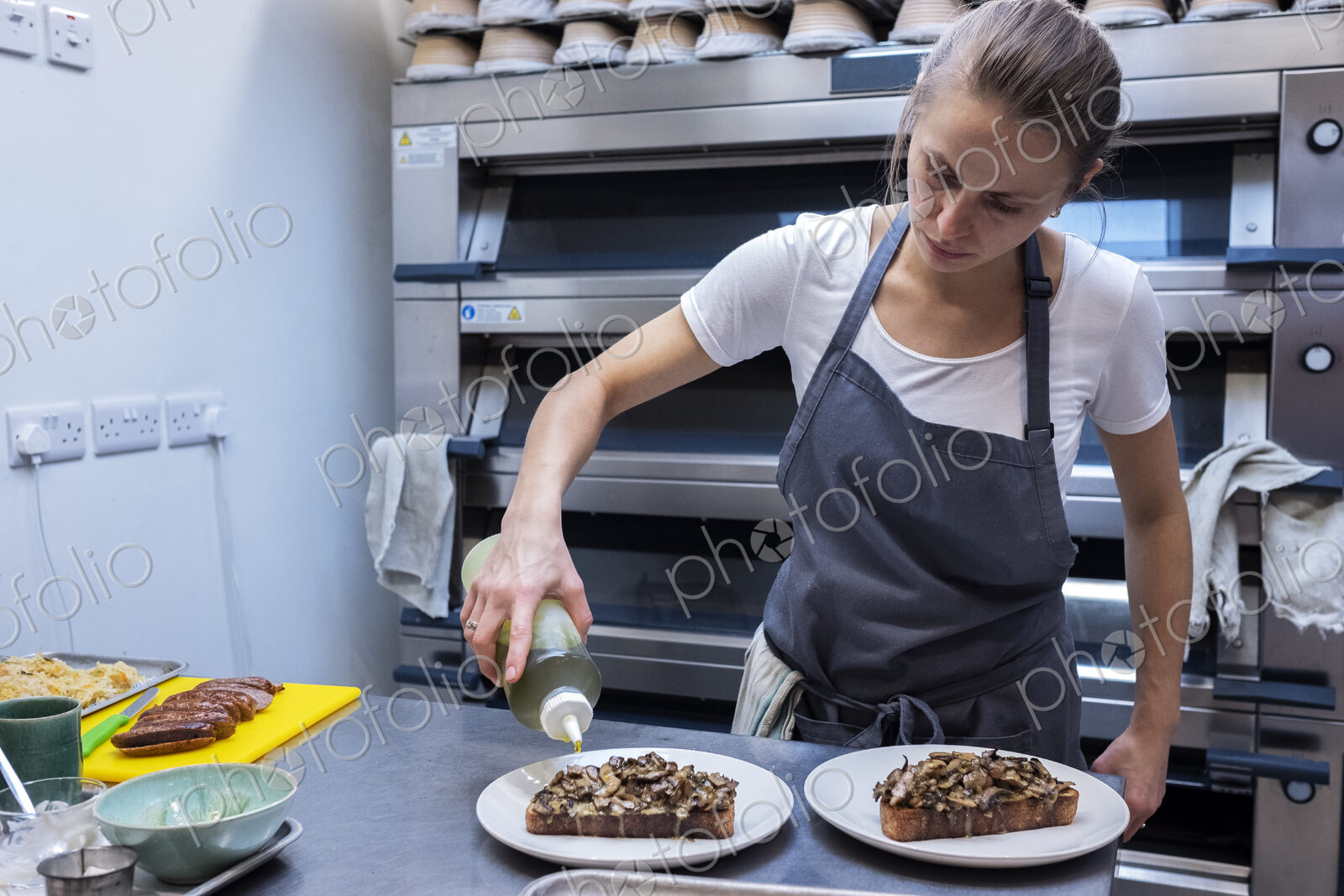 Woman wearing apron standing in an artisan bakery, preparing plate of food.