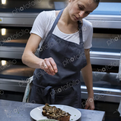 Woman wearing apron standing in an artisan bakery, preparing plate of food. Woman wearing apron standing in an artisan bakery, preparing plate of food.