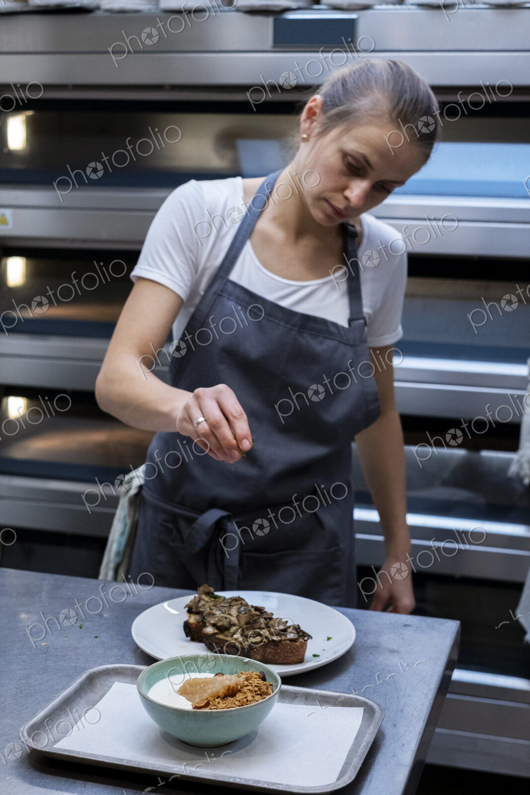 Woman wearing apron standing in an artisan bakery, preparing plate of food.