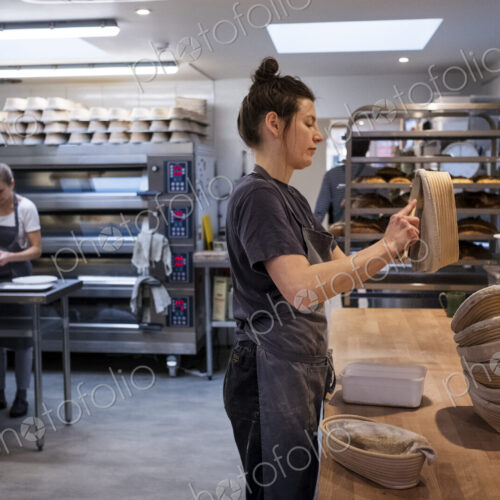 Woman wearing apron standing in an artisan bakery, preparing proving baskets.