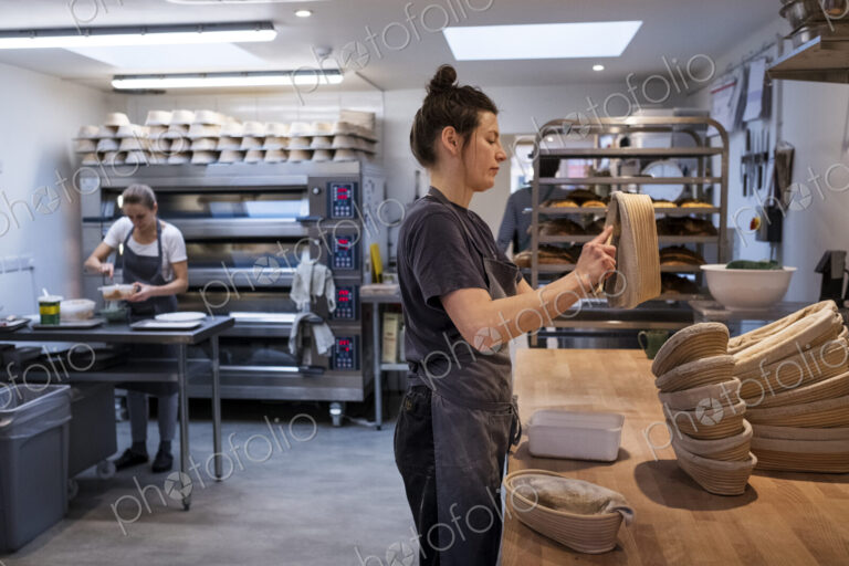 Woman wearing apron standing in an artisan bakery, preparing proving baskets.