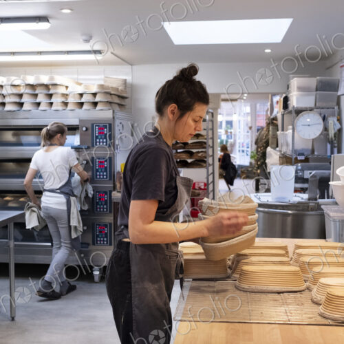 Woman wearing apron standing in an artisan bakery, preparing proving baskets.