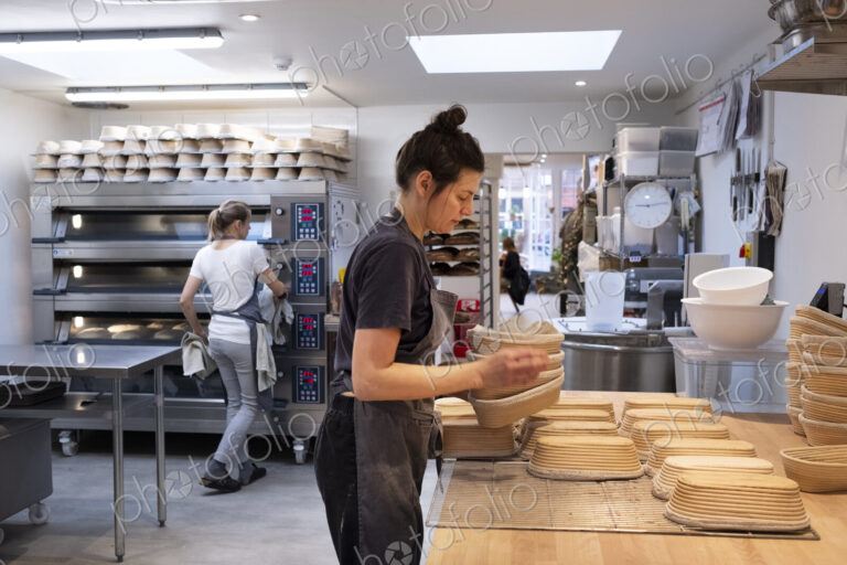 Woman wearing apron standing in an artisan bakery, preparing proving baskets.