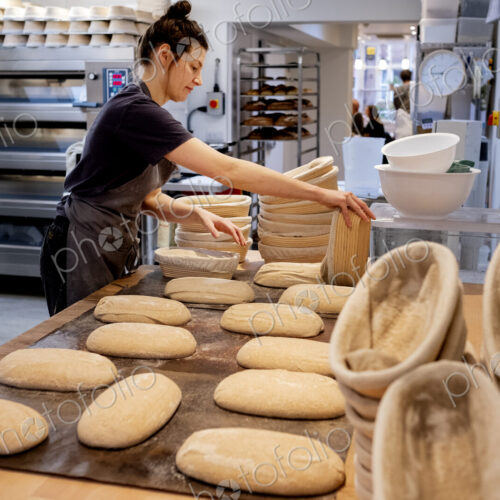 Woman wearing apron standing in an artisan bakery, shaping sourdough loaves for baking.