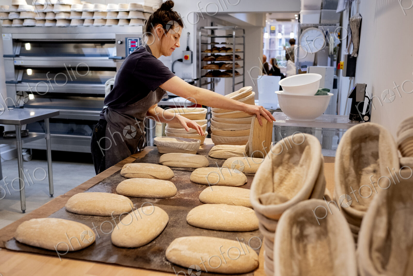 Woman wearing apron standing in an artisan bakery, shaping sourdough loaves for baking.