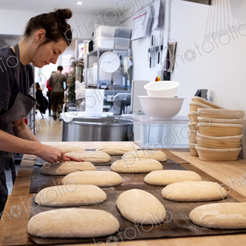 Woman wearing apron standing in an artisan bakery, shaping sourdough loaves for baking.