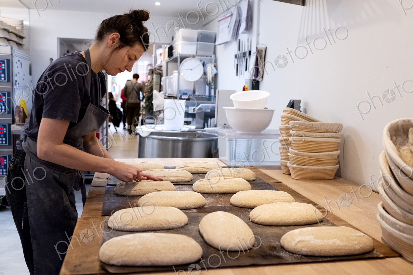 Woman wearing apron standing in an artisan bakery, shaping sourdough loaves for baking.