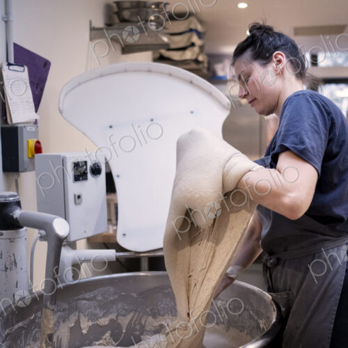 Woman wearing apron standing in an artisan bakery, working with sourdough.