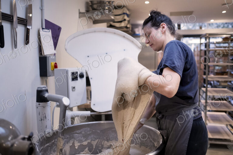 Woman wearing apron standing in an artisan bakery, working with sourdough.