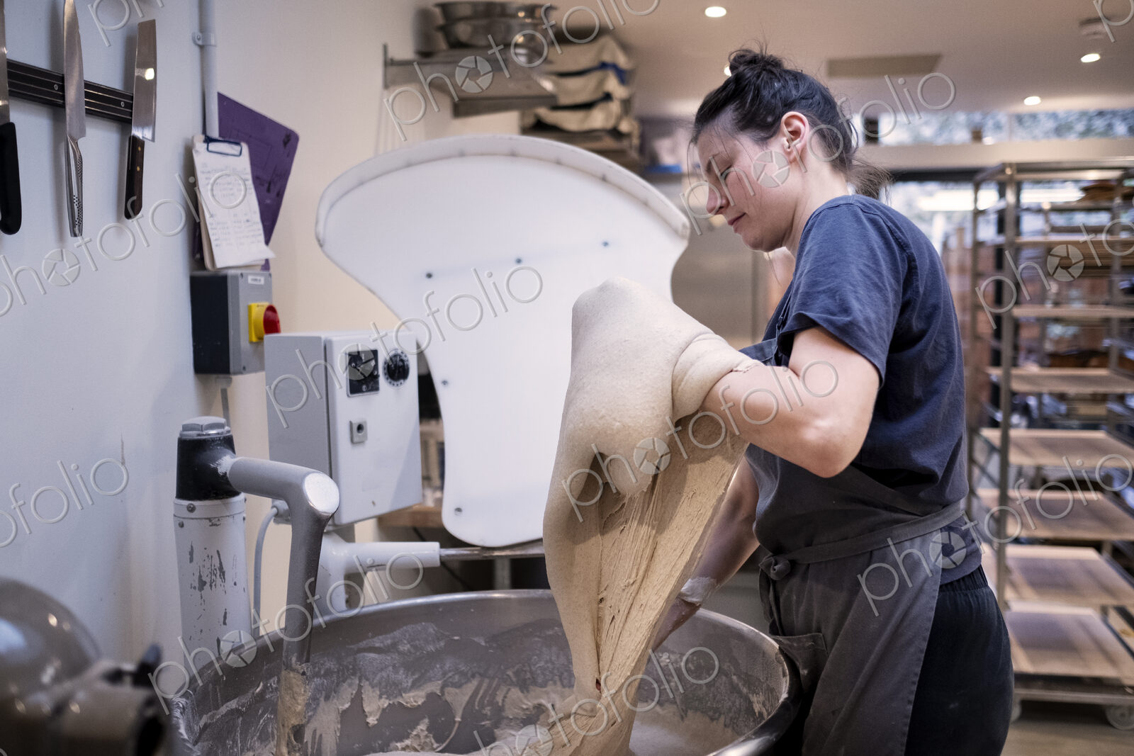Woman wearing apron standing in an artisan bakery, working with sourdough.