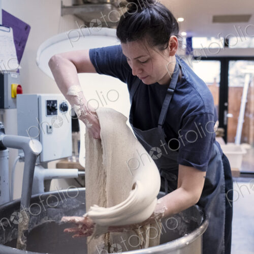 Woman wearing apron standing in an artisan bakery, working with sourdough.