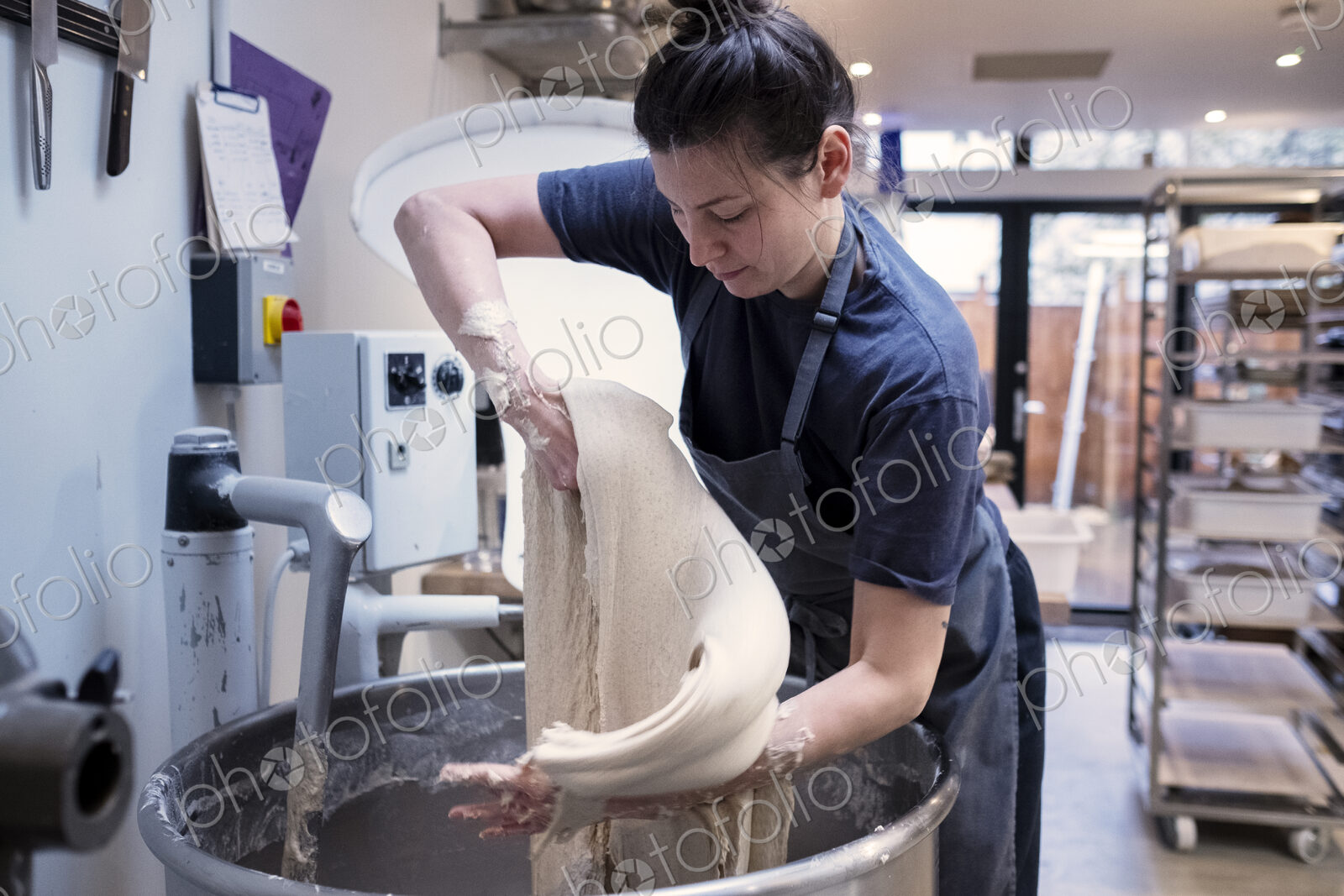 Woman wearing apron standing in an artisan bakery, working with sourdough.