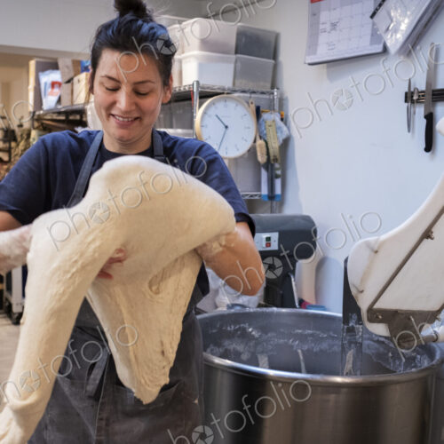 Woman wearing apron standing in an artisan bakery, working with sourdough.