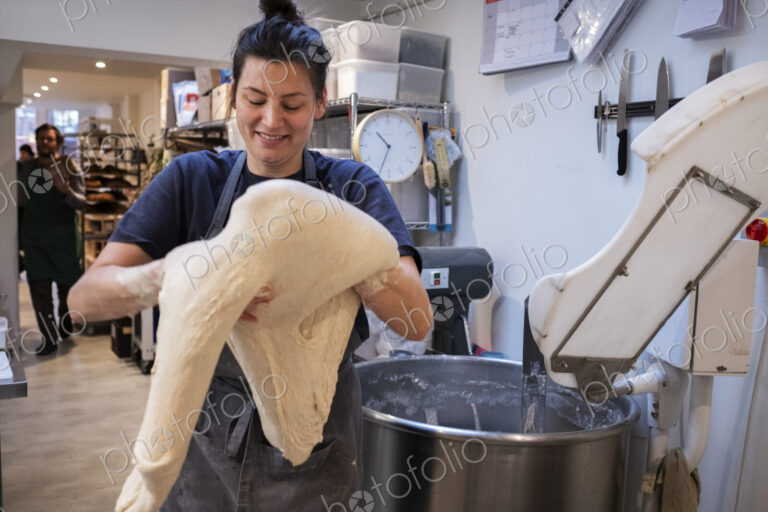 Woman wearing apron standing in an artisan bakery, working with sourdough.