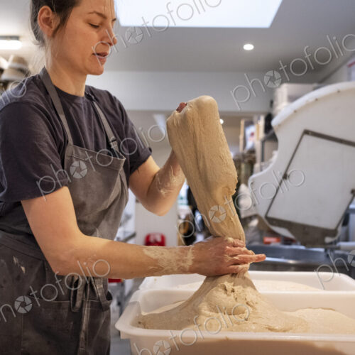 Woman wearing apron standing in an artisan bakery, working with sourdough.