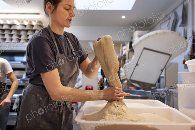 Woman wearing apron standing in an artisan bakery, working with sourdough.