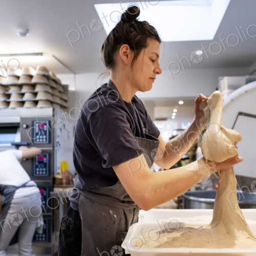 Woman wearing apron standing in an artisan bakery, working with sourdough.