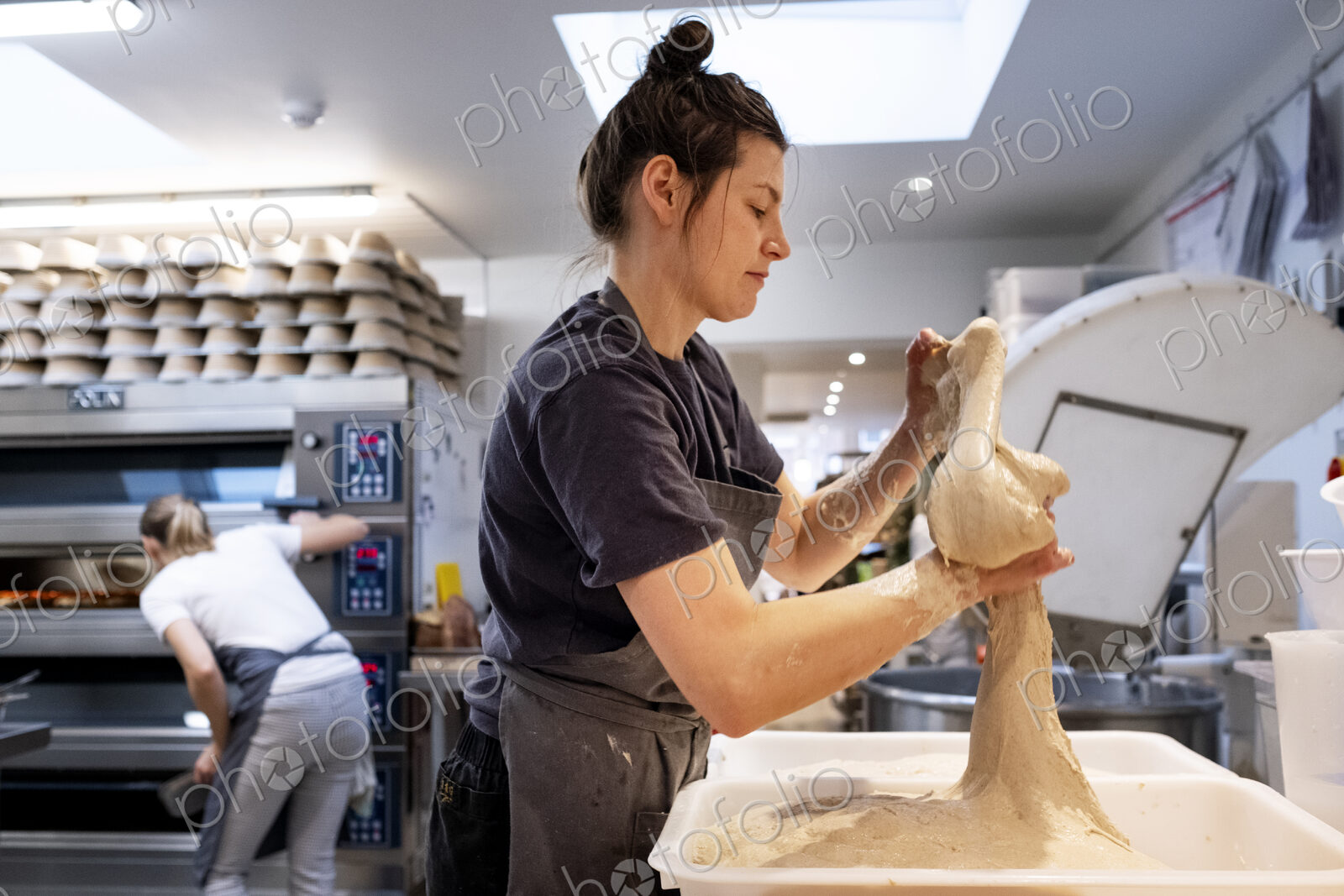 Woman wearing apron standing in an artisan bakery, working with sourdough.