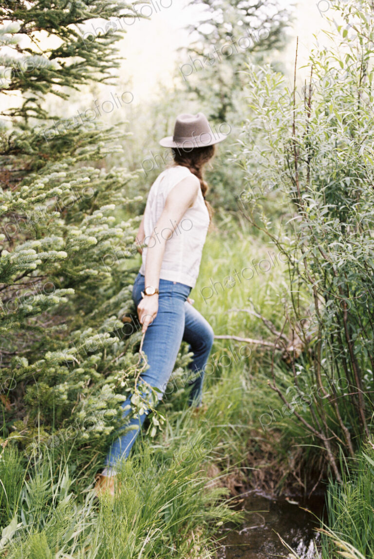 Woman wearing jeans and a hat walking through a forest.